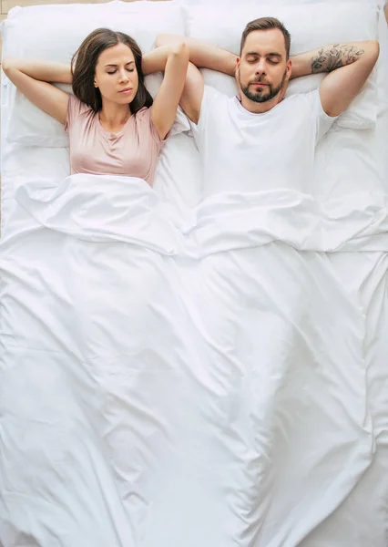 Bedtime. The family are sleeping. Beautiful young couple in love are lying on the big white bed and resting. Husband and wife together in bed. Top view photo