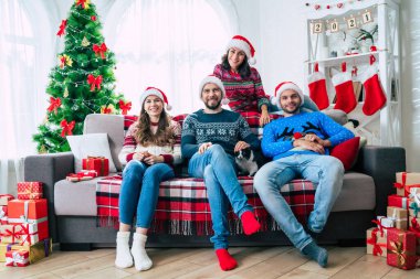 Mutlu Noeller ve mutlu yıllar. Noel Baba şapkalı mutlu genç arkadaşlar kanepede otururken birlikte eğleniyorlar..