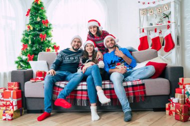 Mutlu Noeller ve mutlu yıllar. Noel Baba şapkalı mutlu genç arkadaşlar kanepede otururken birlikte eğleniyorlar..