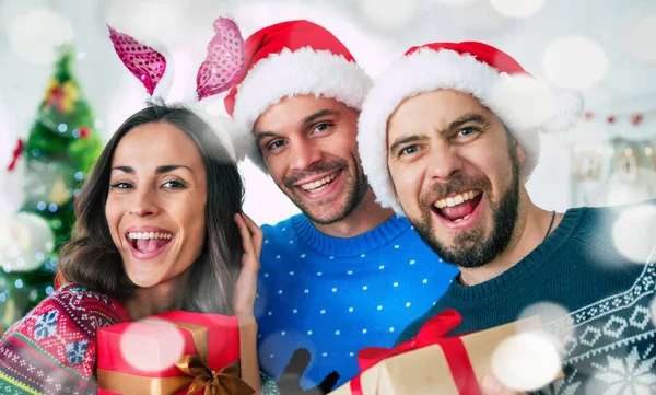 サンタの帽子の興奮した美しい友人の幸せなグループは クリスマスツリーの背景で家でパーティーをしながら楽しんでいます — ストック写真