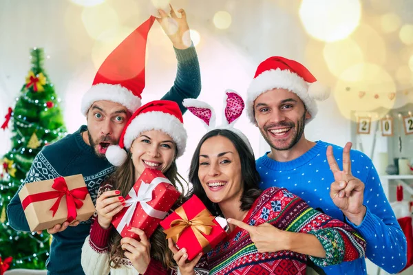サンタの帽子の興奮した美しい友人の幸せなグループは クリスマスツリーの背景で家でパーティーをしながら楽しんでいます — ストック写真