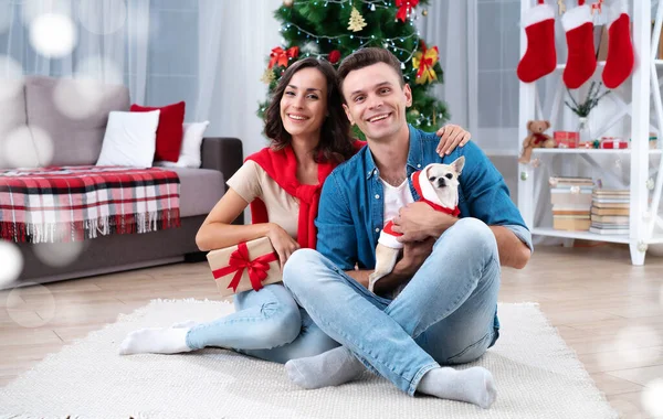Christmas romantic present. Happy beautiful young couple in love are making a surprise and giving gifts for each other while sitting on the floor at home on Christmas tree background.