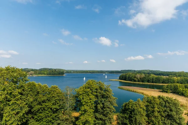 Scenic summer landscape with sailboats on a turquoise lake, surrounded by green forest and blue sky, tranquil nature view, travel destination and outdoor recreation