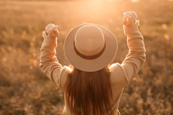 rear view of woman wearing hat in sunset light