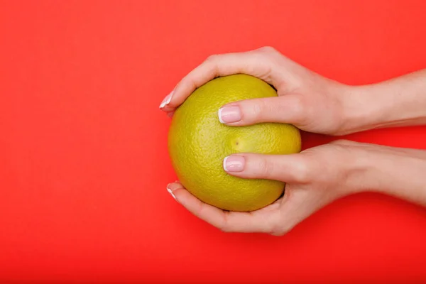 Beautiful female hands with stylish nail manicure gel polish on red background. Top view of grapefruit in hands. Woman files her nails. Free space for text.