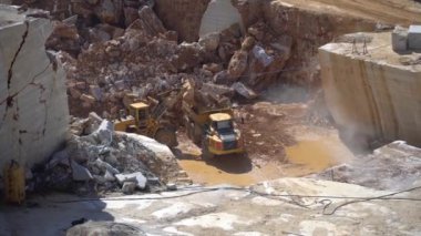 Marmara adası, Türkiye - Mayıs 2019: Ağır inşaat kamyonuna mermer parçaları yükleyen ekskavatör aracı