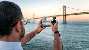 Bir fotoğrafçı Dji Osmo Pocket 'i San Francisco, Usa' daki Bay Bridge 'in görüntülerini çekmek için kullanıyor.