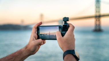 Bir fotoğrafçı Dji Osmo Pocket 'i San Francisco, Usa' daki Bay Bridge 'in görüntülerini çekmek için kullanıyor.