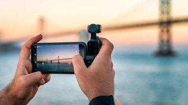 Bir fotoğrafçı Dji Osmo Pocket 'i San Francisco, Usa' daki Bay Bridge 'in görüntülerini çekmek için kullanıyor.