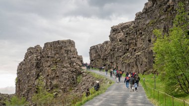 İzlanda 'daki Thingvellir Milli Parkı' ndaki tektonik plakalar ve dere arasında yürüyen insanlar.