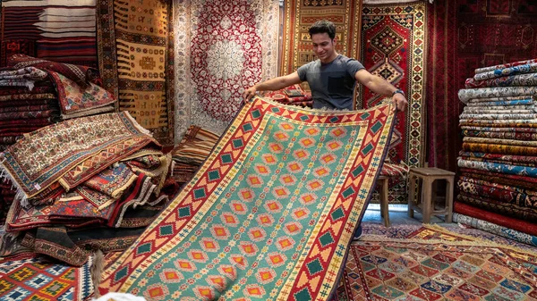 Joven vendedor de alfombras iraní presentando alfombras persas a los turistas en una tienda de alfombras, Isfihan, Irán — Foto de Stock