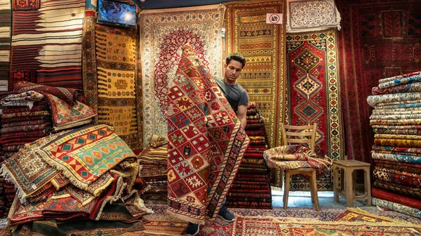 Joven vendedor de alfombras iraní presentando alfombras persas a los turistas en una tienda de alfombras, Isfihan, Irán — Foto de Stock