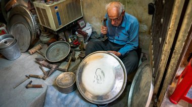 Yaşlı İranlı adam çekiçle çeşitli eski aletlerle bir mağazada çalışıyor, Yazd, İran