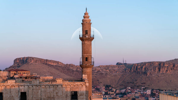 Mardin, Turkey - January 2020: Sehidiye mosque and its minaret with moon rising Mardin old city cityscape