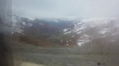 Yağmur damlaları ve karlı bir araba penceresinin arkasındaki bulanık kış manzarası. Pencereye odaklanmak kasıtlı olarak yapılır. Bitlis, Doğu Türkiye