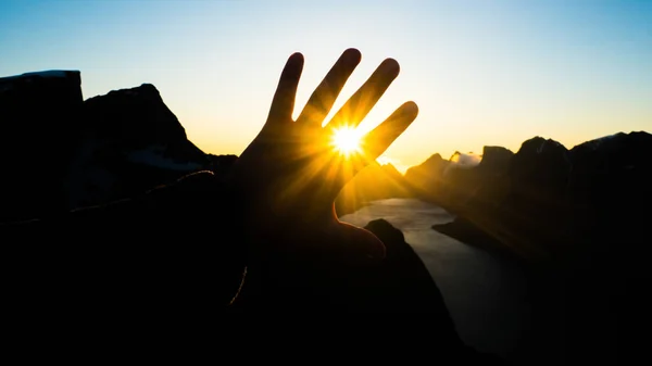 Hand reaching out for midnight sun in Norway. The sun doesnt set during summer months in Norway and the sun is still shining in midnight.