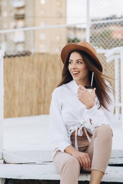 Şık bir kadın kahve içiyor ve gün batımında sıcak bir yaz gününde sahilde yürüyor.