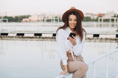 Şık bir kadın telefonda konuşuyor ve sıcak bir yaz günü gün batımında sahilde yürüyor.