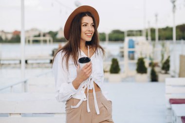 Şık bir kadın kahve içiyor ve gün batımında sıcak bir yaz gününde sahilde yürüyor.