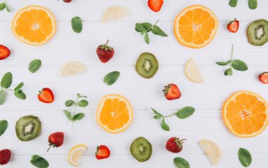 Renkli yaz yatağı. Turunçgillerden, yeşil kivilerden, beyaz ahşap masada yapraklardan ve çileklerden oluşan desen..