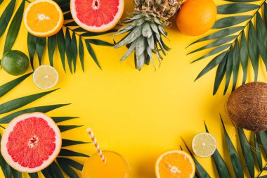 Yaz meyveleri. Tropik palmiye yaprakları, ananas, hindistan cevizi, greyfurt, portakal ve sarı arka planda bir bardak meyve suyu. Düz konum, üst görünüm, kopyalama alanı