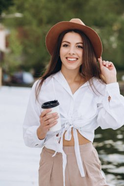 Şık bir kadın kahve içiyor ve gün batımında sıcak bir yaz gününde sahilde yürüyor.