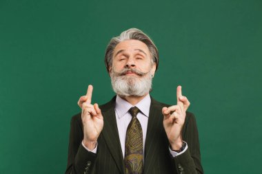 Sakallı, orta yaşlı bir adam yeşil arka planda şans dilemek için dua ediyor..