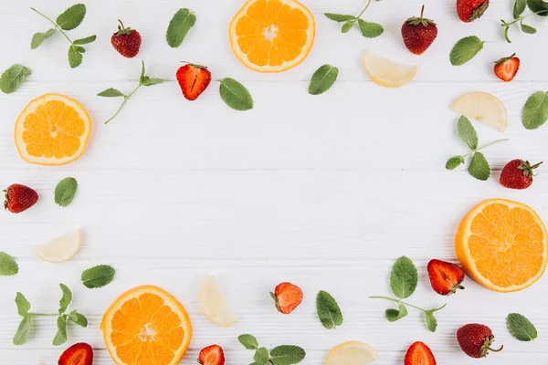 Summer colorful flat lay. Pattern made of citrus fruits, leaves and strawberries on the white wooden table. Top view and copy space