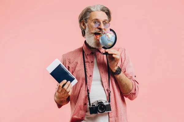 Happy bearded man in sunglasses with a camera and passport chooses a country on a globe for travel.