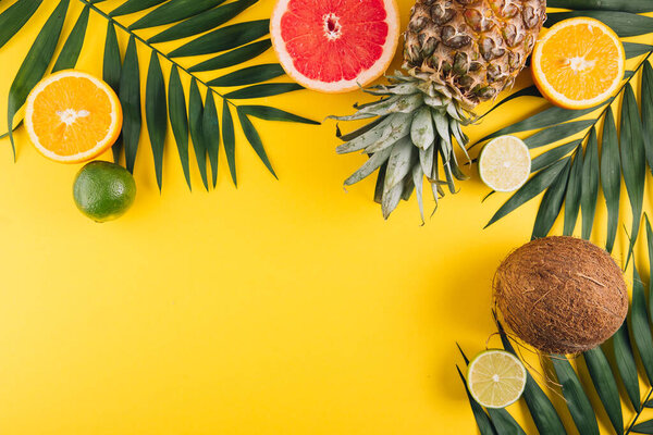 Летние фрукты. Тропические пальмовые листья, ананас, кокос, грейпфрут, оранжевый и лайм на желтом фоне. Плоская кладка, вид сверху, копировальное пространство
