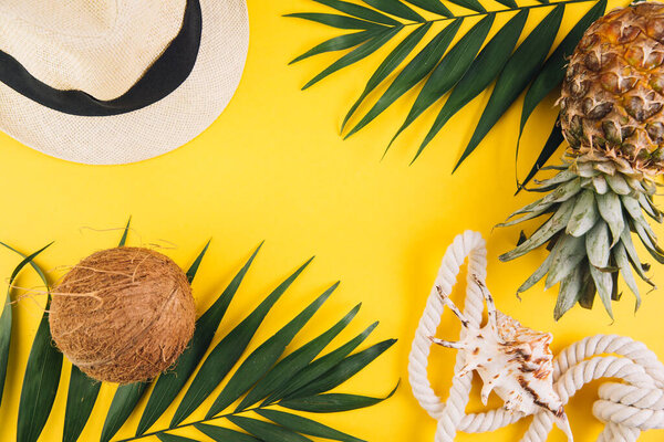 Summer flat lay background. Palm leaves, coconut, pineapple, sunglasses, rope, straw hat and shell on yellow background.