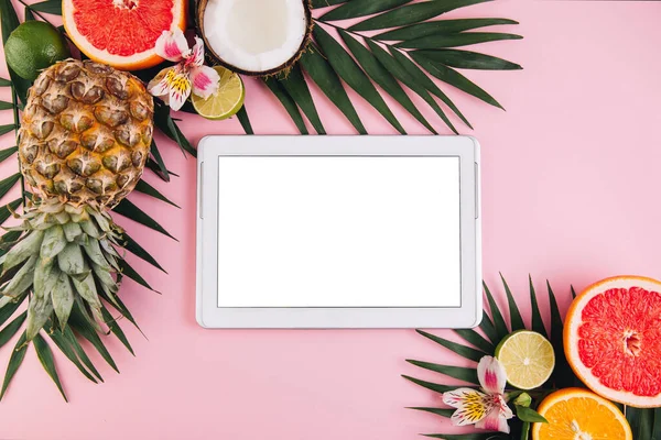 Tablet frame around summer fruit composition on pink table. Flat lay, top view, copy space