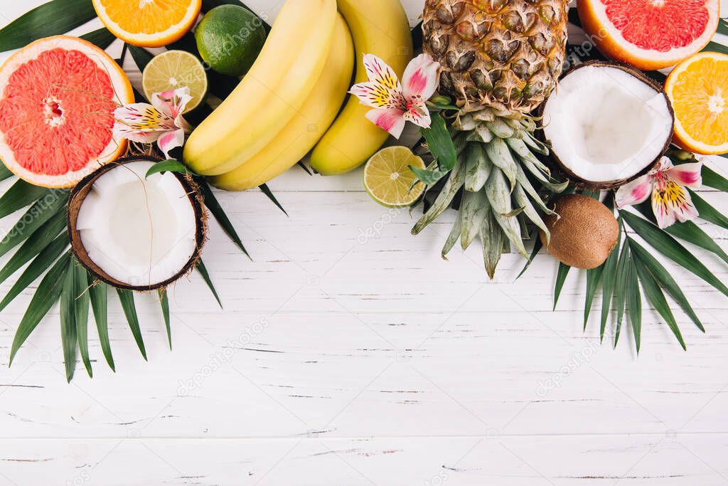 Summer fruits. Tropical palm leaves, pineapple, coconut, grapefruit, orange and bananas on wooden background. Flat lay, top view, copy space