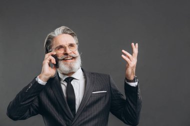 İş dünyası ve modaya uygun sakallı, gri takım elbiseli, gülümseyen, telefonla konuşan ve gri arka planda fotokopi çeken olgun bir adam..