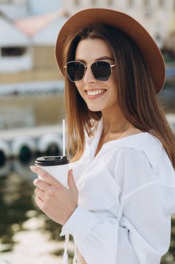 Şık bir kadın kahve içiyor ve gün batımında sıcak bir yaz gününde sahilde yürüyor.