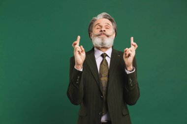 Sakallı, orta yaşlı bir adam yeşil arka planda şans dilemek için dua ediyor..