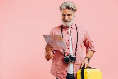 Sakallı şık adam sarı bir bavul tutuyor ve haritada seyahat etmek için bir ülke seçiyor..