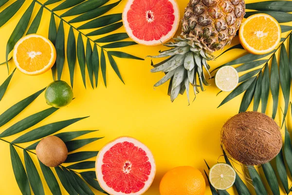 Summer fruits. Tropical palm leaves, pineapple, coconut, grapefruit, orange and lime on yellow background. Flat lay, top view, copy space