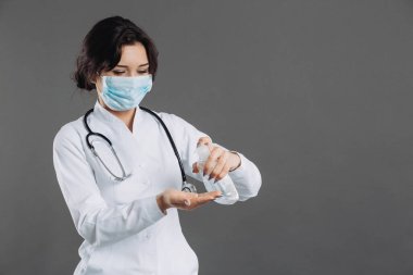 Cerrahi maske takan doktor alkol jeli pompa şişesini gösteriyor. Alkol jeliyle ya da antibakteriyel sabun dezenfektanıyla ellerini yıkamak. Covid-19 veya Coronavirus konsepti.