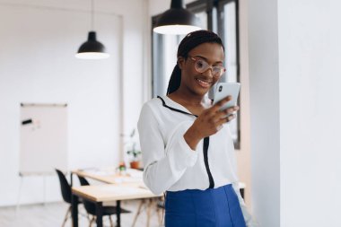 Güzel Afrikalı şirket çalışanı modern ofiste cep telefonuyla konuşuyor.