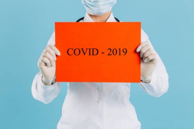 Cerrahi maskeli doktor kadın kırmızı kağıda işaret ediyor. Mesaj Coronavirus, mavi arka planda izole edilmiş.