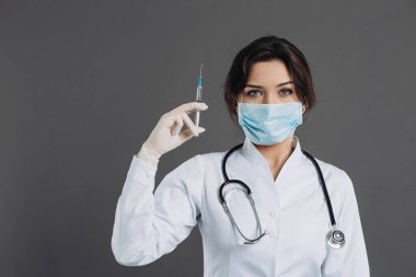Steteskoplu kadın doktor, elinde enjeksiyon var, gri arka planda koronavirüse karşı panzehir. covid-2019 kavramı