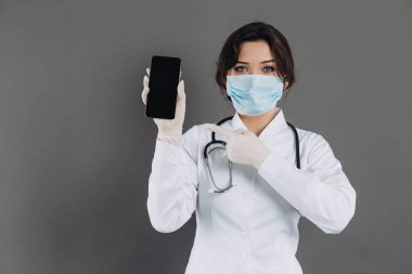 Stetoskop maskesi takan kadın doktor elinde akıllı bir telefon tutuyor ve bir şey gösteriyor. covid-19 kavramı