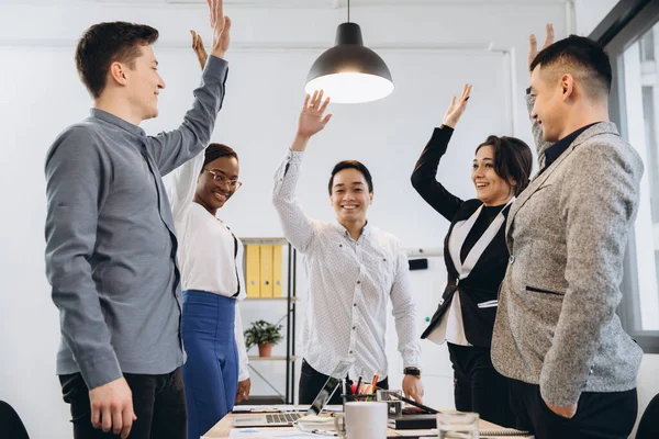 Multiracial euphoric business team people give high five at office table, happy excited diverse work group engaged in teambuilding celebrate corporate success win partnership power teamwork concept