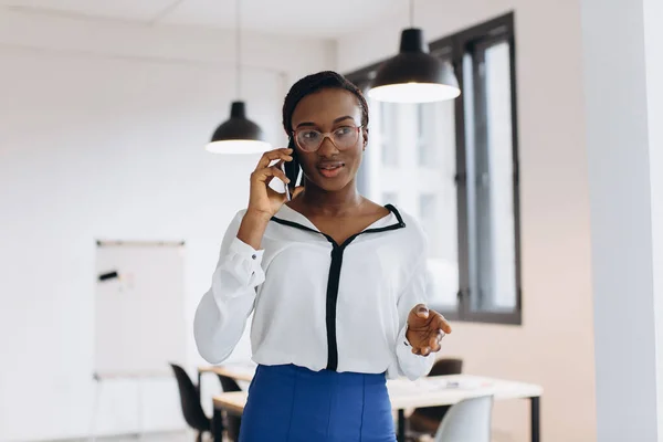 Beautiful african corporate worker talking on mobile phone in modern office