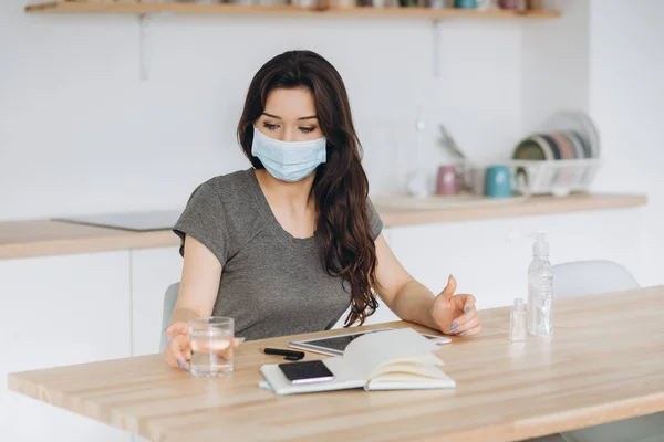 Coronavirus. Young business woman working from home wearing protective mask. Girl in quarantine for coronavirus wearing protective mask. Working from home with sanitizer gel and water