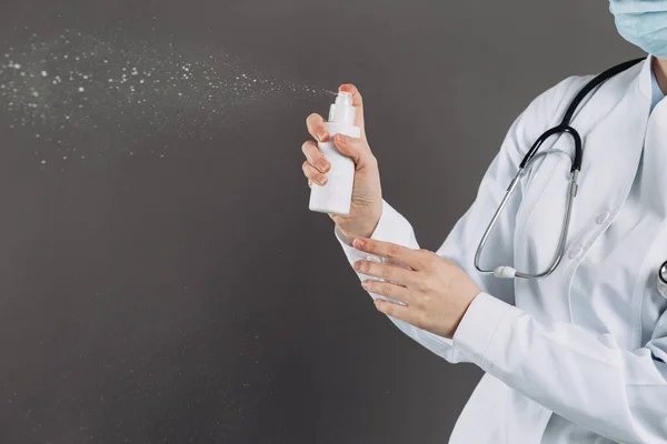 Doctor wearing surgical face mask holding showing alcohol spray pump bottle. Washing hands with alcohol spray or antibacterial soap sanitizer. Covid-19 or Coronavirus concept.