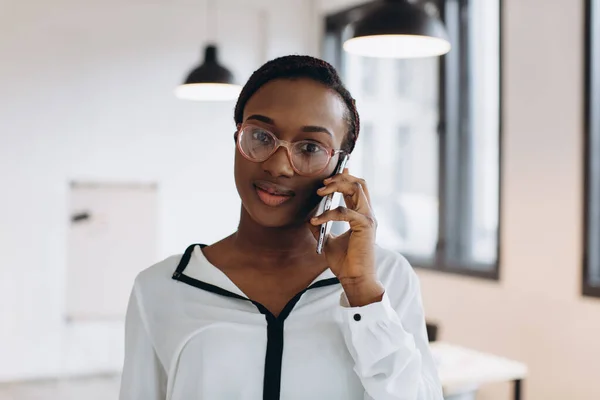 Beautiful african corporate worker talking on mobile phone in modern office