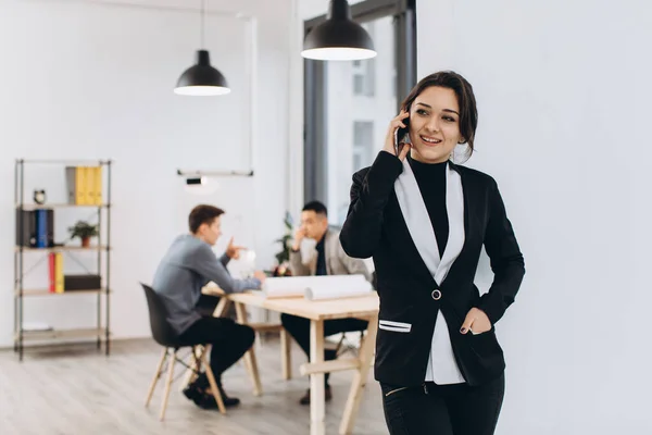 Business woman with mobile phone, people group in background at modern bright office indoors