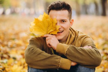 Bir buket sarı yapraklı yakışıklı ve mutlu çocuğun portresi gülerek sonbahar parkında hayal kuruyor.